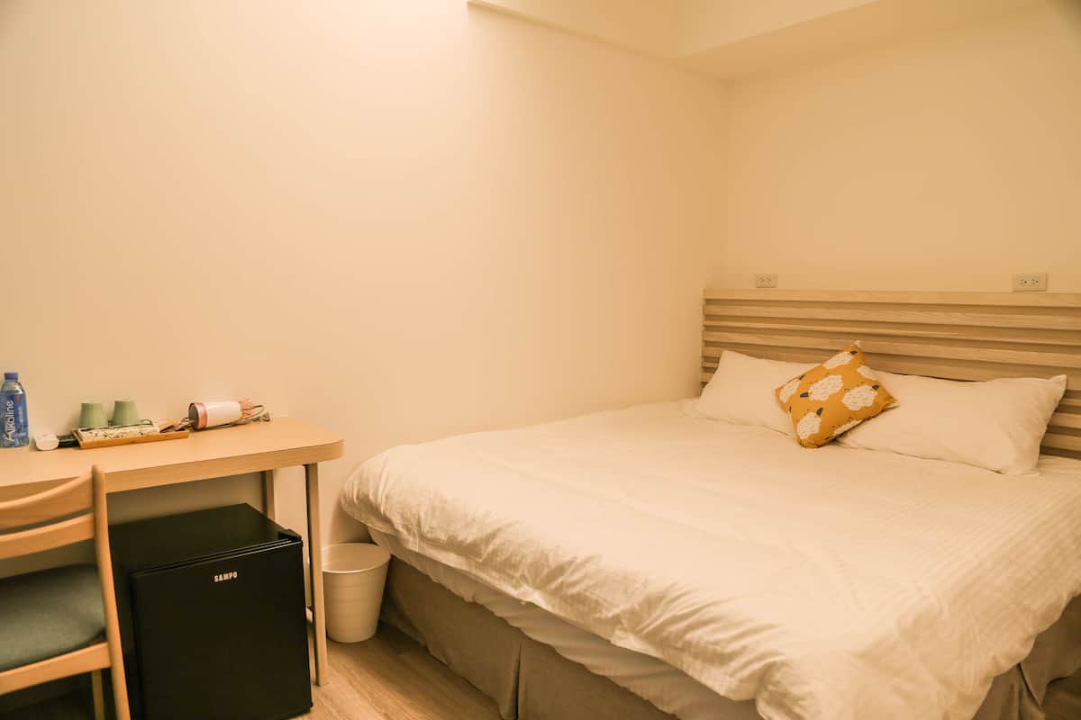 Un dormitorio ordenado con una cama, un escritorio y un mueble negro para guardar objetos.