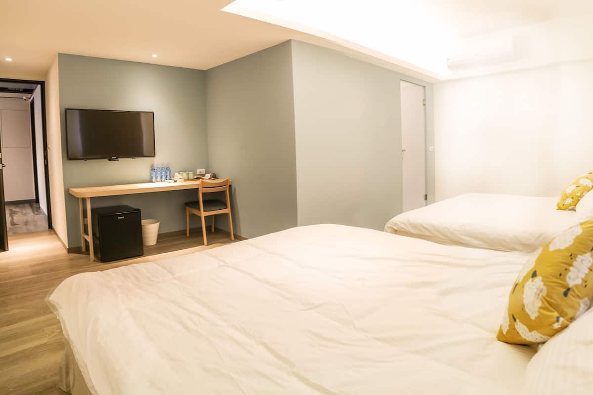Una habitación de hotel con dos camas, un escritorio, una silla, un televisor y un cubo de basura.
