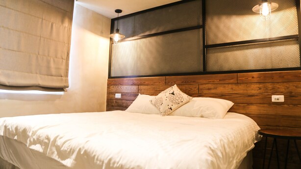 Un dormitorio con cabecera de madera, cama con ropa de cama blanca y una pequeña mesa redonda.