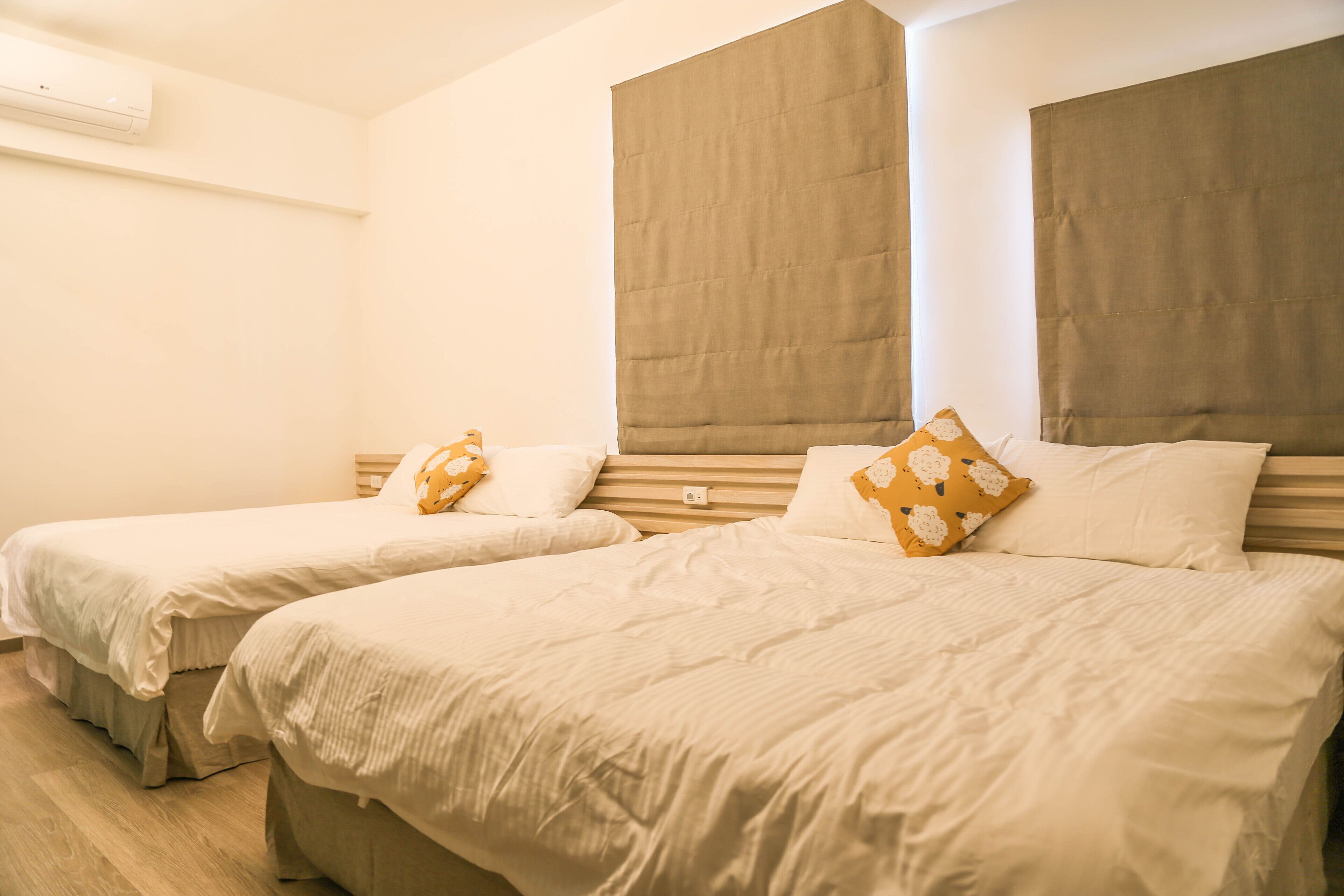 Two single beds with headboards, a wooden floor, and a wall-mounted air conditioner.
