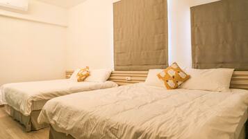 Two single beds with headboards, a wooden floor, and a wall-mounted air conditioner.