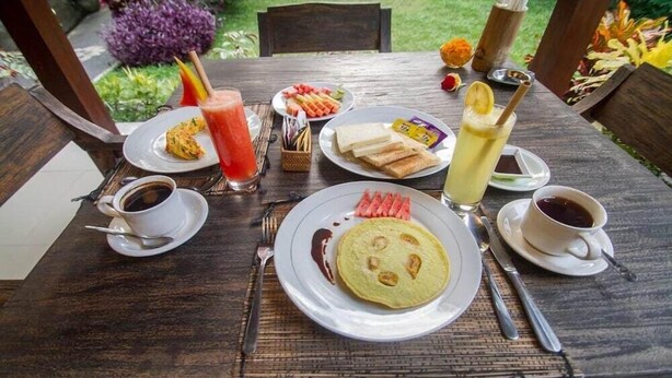 A wooden table with breakfast items including pancakes, toast, and a drink. - ADI JAYA COTTAGES (Ubud)
