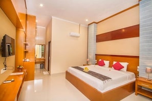 A modern hotel room with a large bed, a wooden desk, a television, and a bathroom visible through an open door. - ADI JAYA COTTAGES (Ubud)