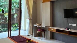 A modern hotel room with a large bed, a desk, a chair, and a TV. - ADI JAYA COTTAGES (Ubud)