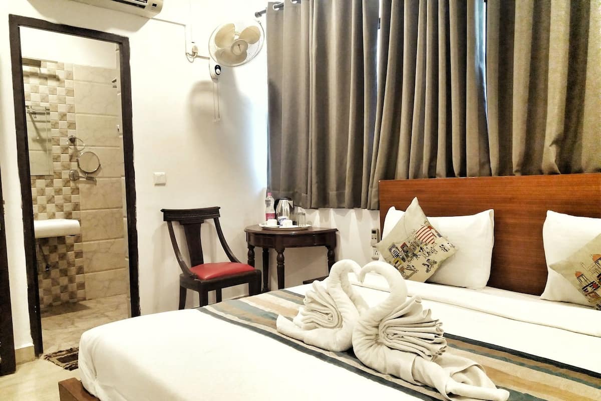 A hotel room with a bed, a chair, a small table with a kettle, and a shower area.