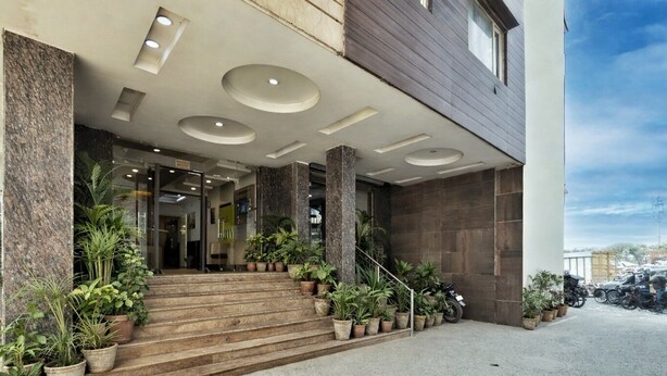 Entrada de un edificio con escaleras, plantas en macetas y cielo despejado.