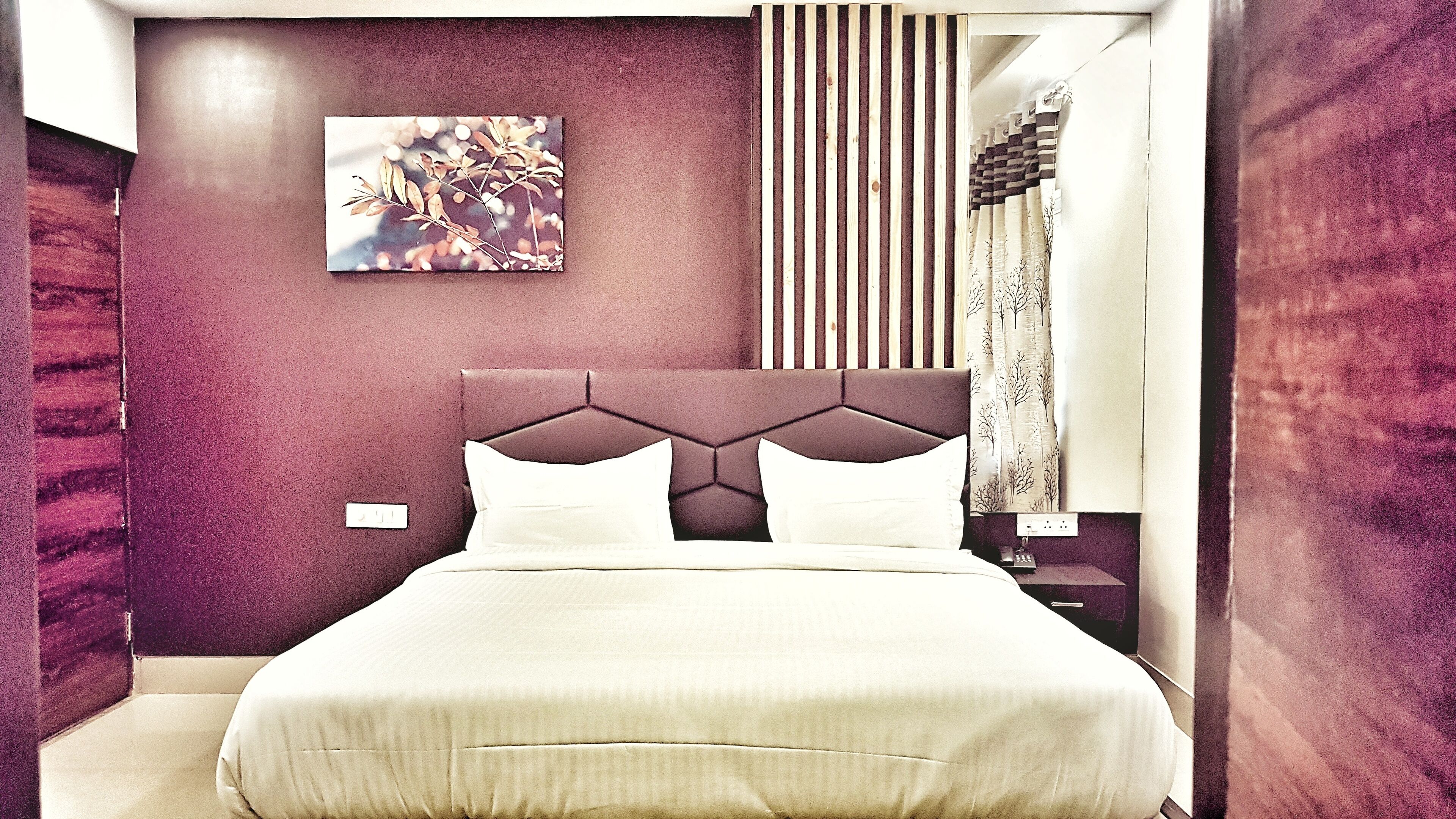 Ein modernes Schlafzimmer mit einem großen Bett, einem Kopfteil mit geometrischen Mustern, einem Wandbild und einem Streifenvorhang.