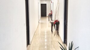 Un pasillo con suelo pulido, una puerta al final y una mesa con planta en la derecha.