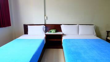 A hotel room with two single beds, each with a blue bedspread and white pillows. There is a wooden nightstand between the beds with a green telephone and a small table.