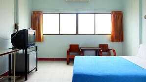 Quarto de hotel com uma cama, uma escrivaninha com televisão, frigorífico, duas cadeiras e uma janela com cortinas.