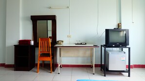 Quarto com escrivaninha, cadeira, televisão e um pequeno frigorífico.