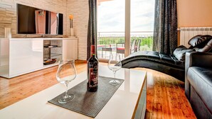 A modern living room with a flat-screen TV, a sofa, a coffee table, and a balcony with outdoor furniture.