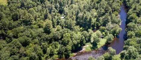 Une vue aérienne d’une zone boisée, avec une rivière, un petit bâtiment et un ciel dégagé.
