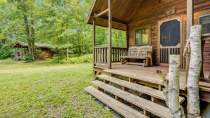 A wooden cabin with a porch, a bench, and a view of the surrounding forest.