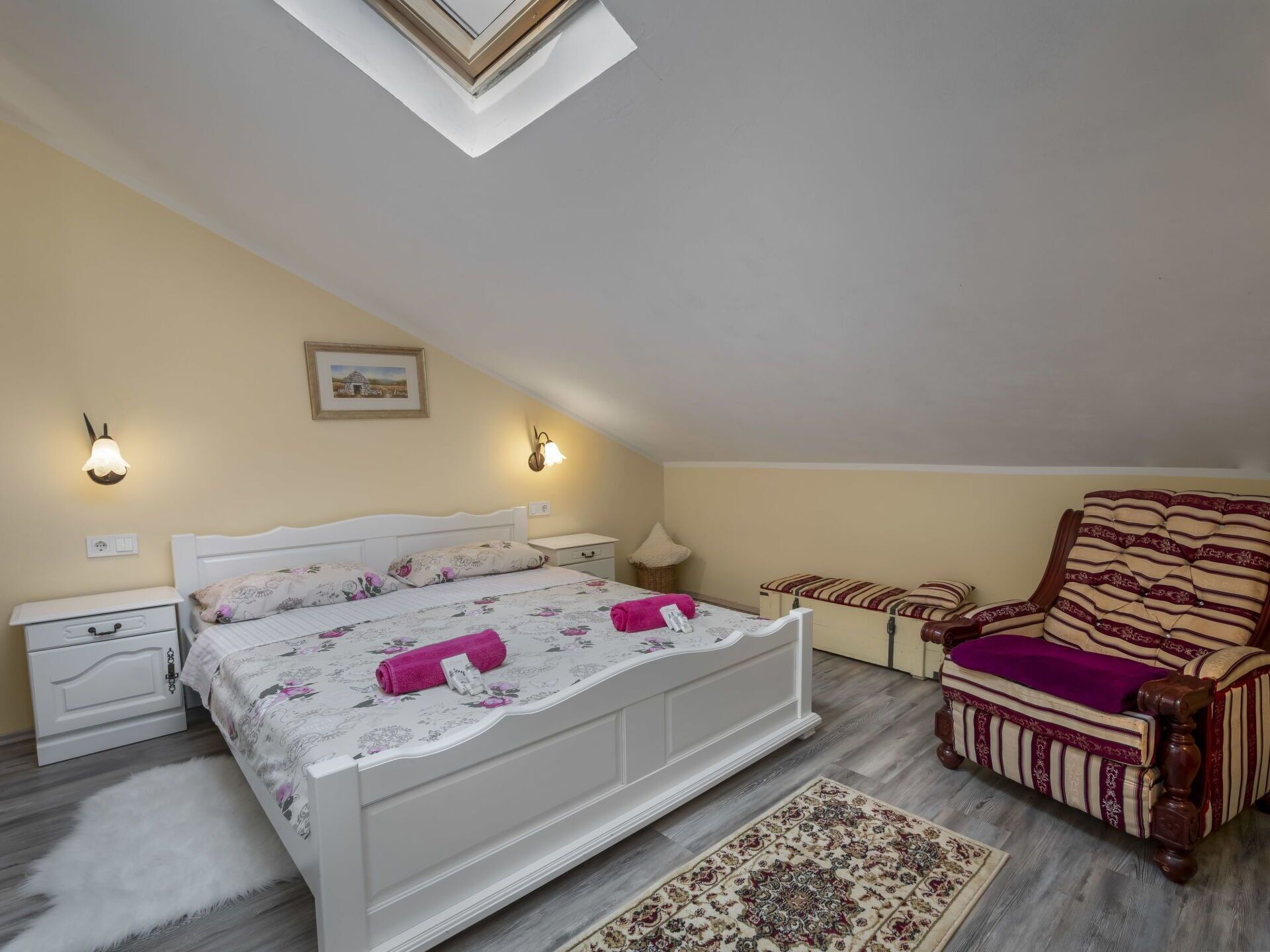 Ein Schlafzimmer mit Bett, Nachttisch, Stuhl, Teppich und einem Bild an der Wand.
