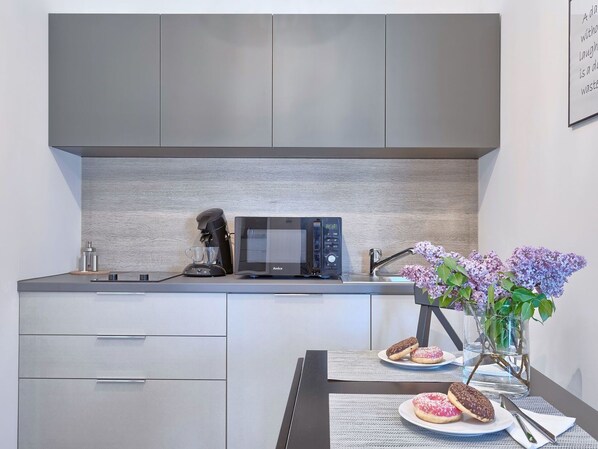 Una cocina moderna con armarios grises, una cafetera, un microondas y una mesa con un florero y donas.
