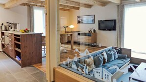 Ein gemütliches Wohnzimmer mit Holzboden, einem Fernseher, einem Essbereich mit Tisch und Stühlen sowie einer Küchenzeile mit Arbeitsplatte und Geräten.