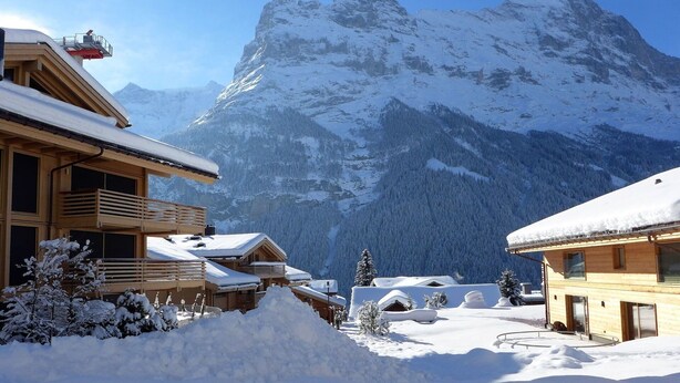 Ein schneebedecktes Berghotel mit Holzbauweise, einem Balkon und Blick auf die umliegenden Berge.
