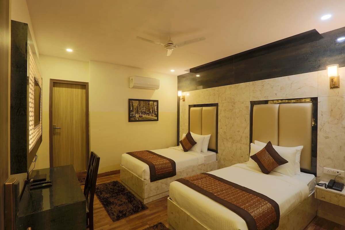 A hotel room with two single beds, a desk with a chair, a ceiling fan, an air conditioning unit, and a wall-mounted light fixture.
