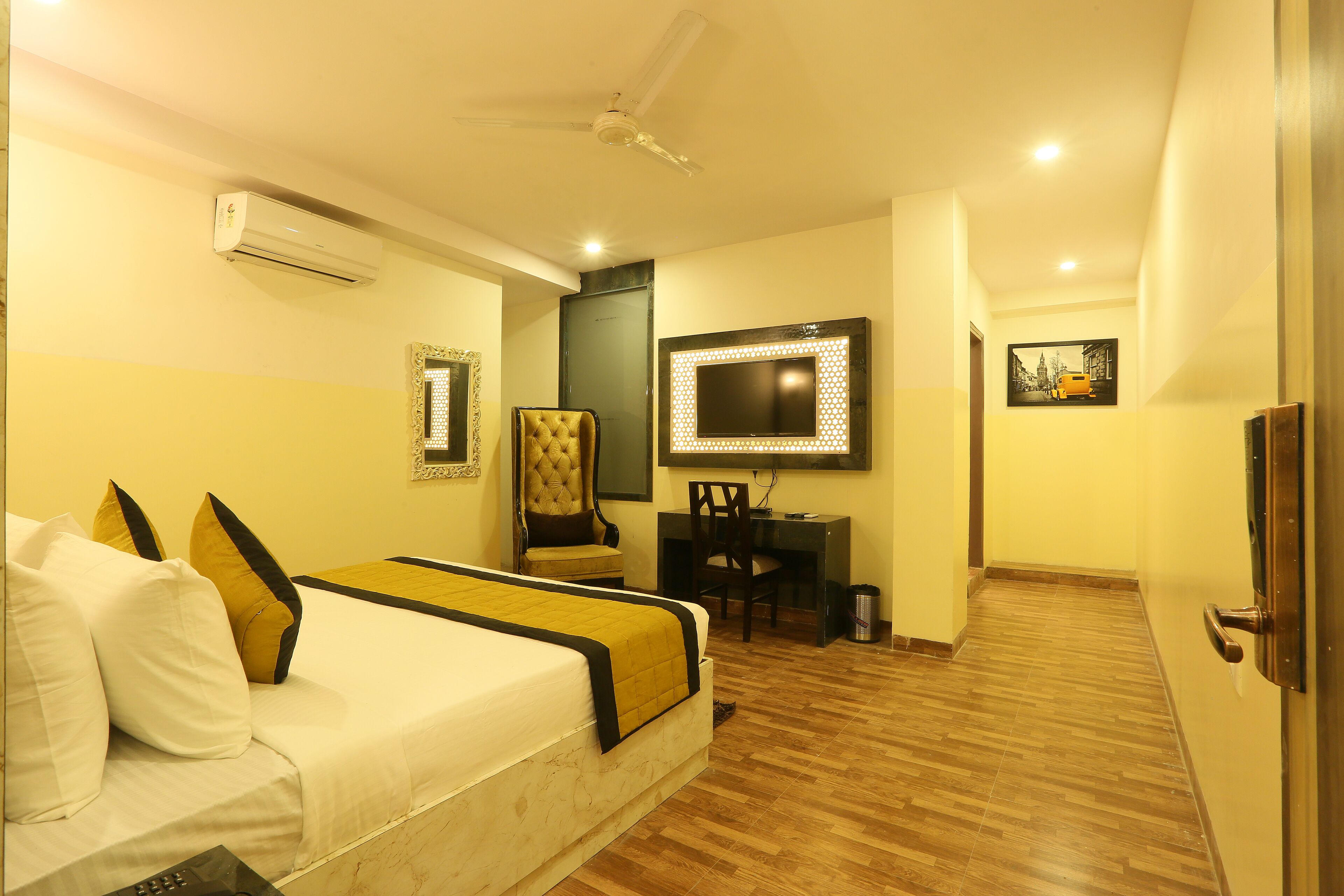 A hotel room with a bed, a desk with a computer, a TV, and an air conditioning unit.