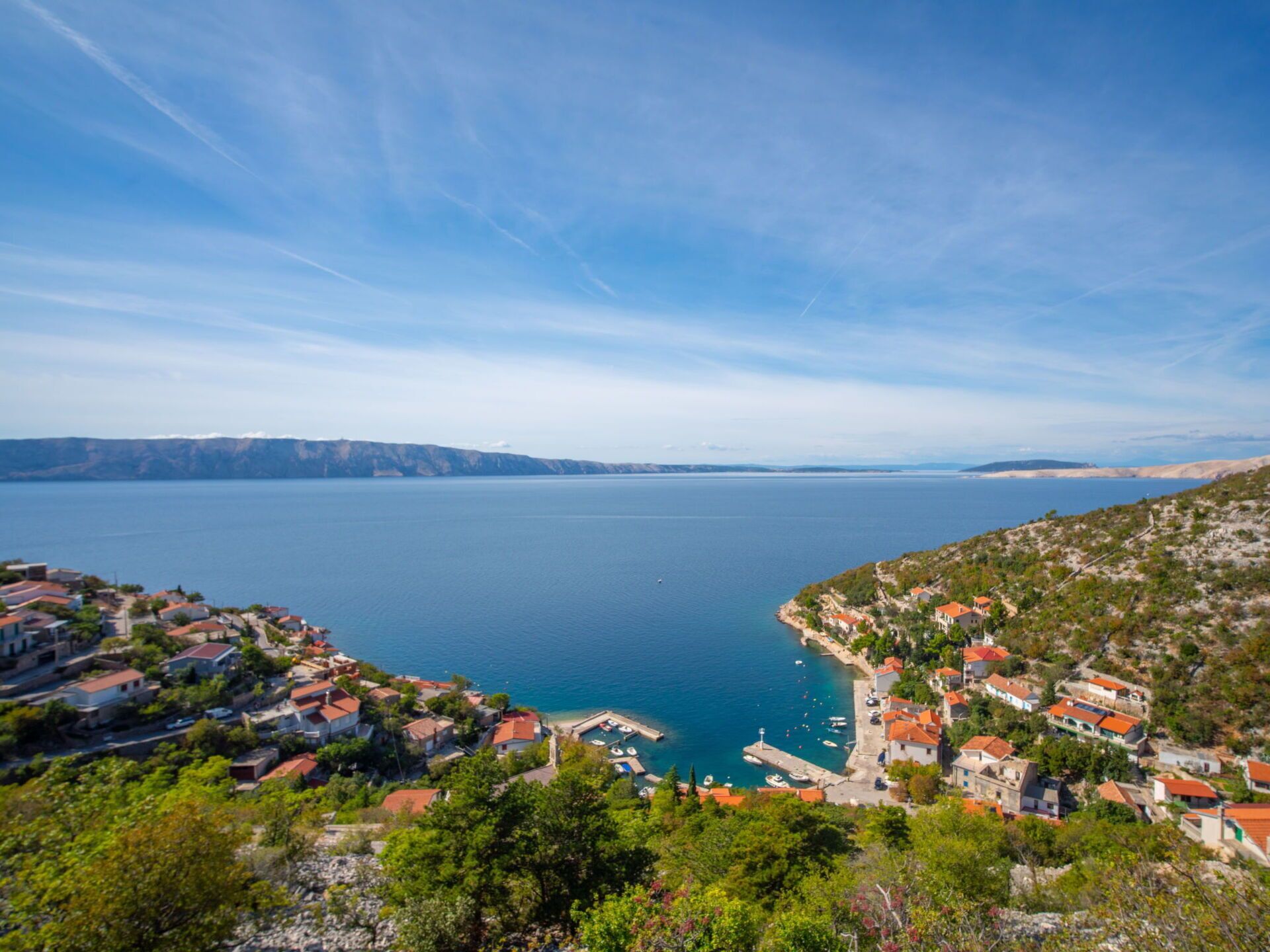 Eine Küstenstadt mit Häusern entlang der Uferlinie, einem klaren blauen Meer und Bergen in der Ferne.