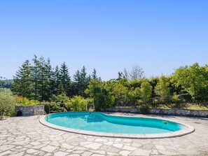 Una piscina con bordo in pietra, circondata da alberi e un muro in pietra.