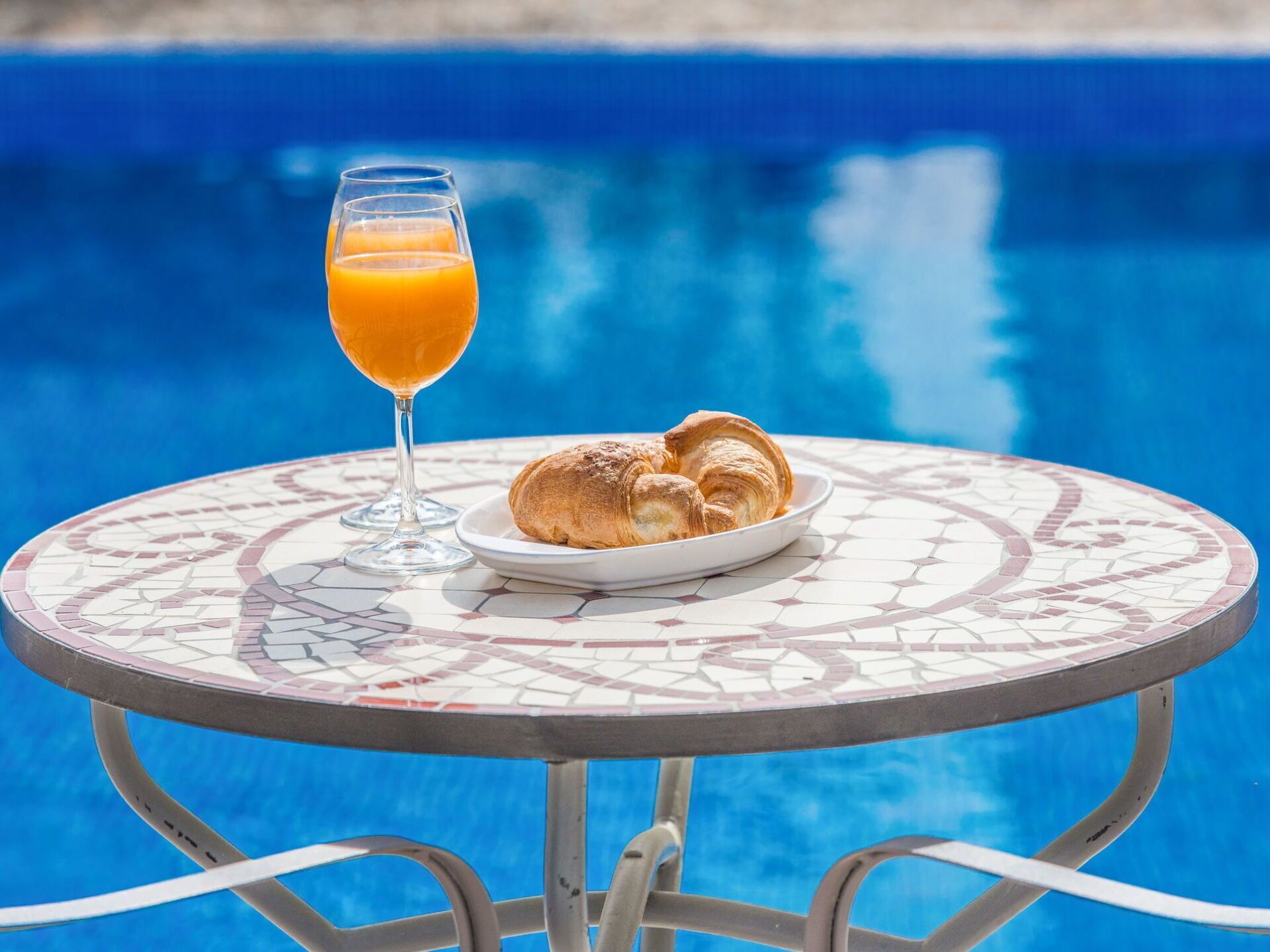 Une table avec un verre de jus d’orange et des croissants, près d’une piscine.