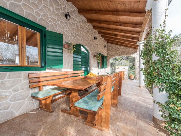 Un bâtiment rustique en pierre, avec des bancs en bois et une table, des volets verts et un mur en pierre.