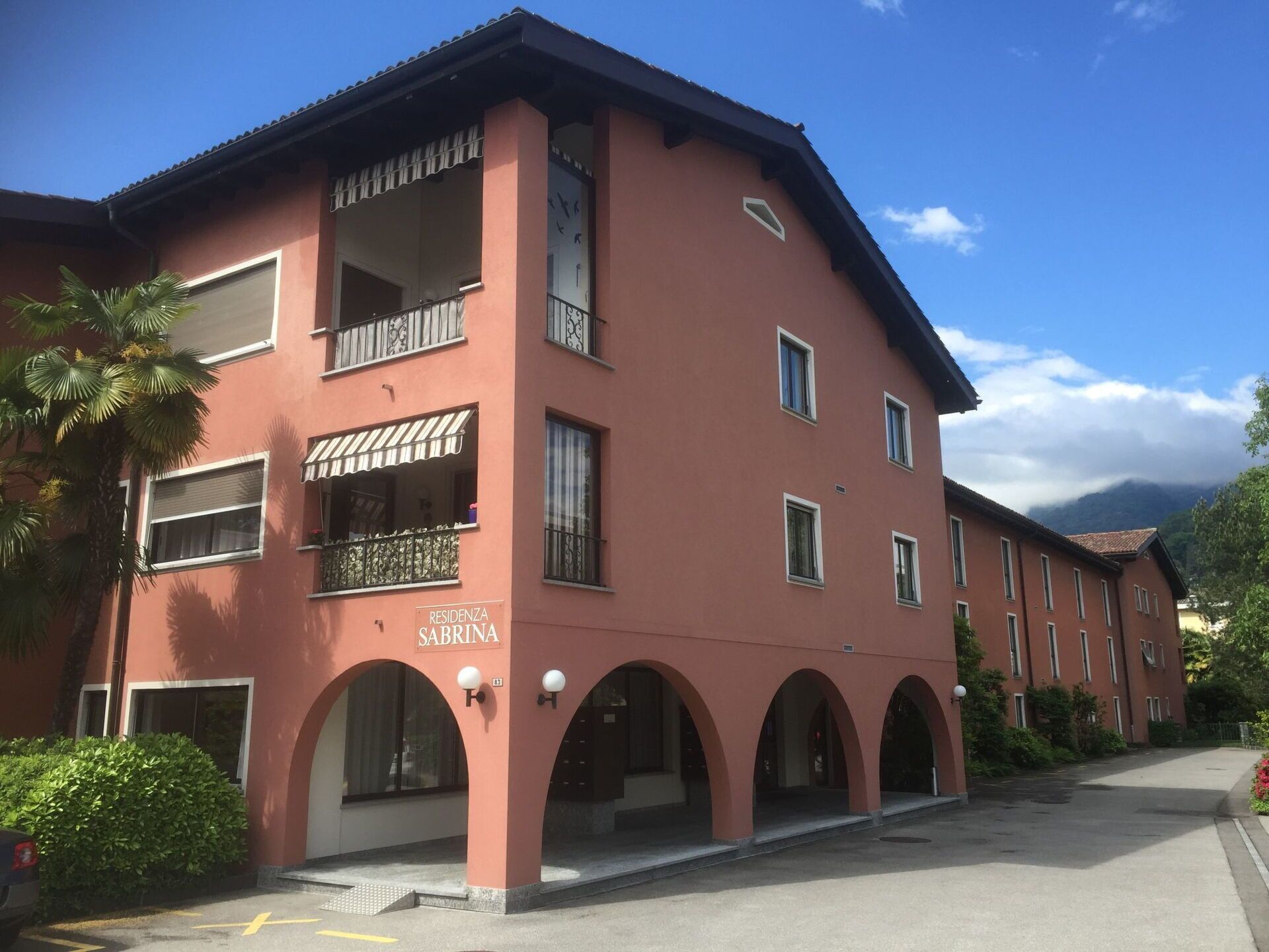 A two-story building with a red facade, multiple balconies, and a sign reading "RESIDENZA SABRINA".