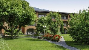 Une cour d’hôtel avec un chemin en pierre, une végétation luxuriante et un bâtiment doté de nombreux balcons.