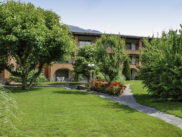 A hotel courtyard with a stone pathway, lush greenery, and a building with multiple balconies.