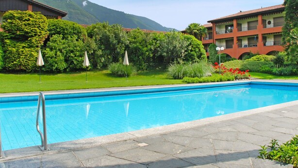 Une piscine dotée d’une plage en pierre, entourée d’une végétation luxuriante et avec une chaîne de montagnes en toile de fond.