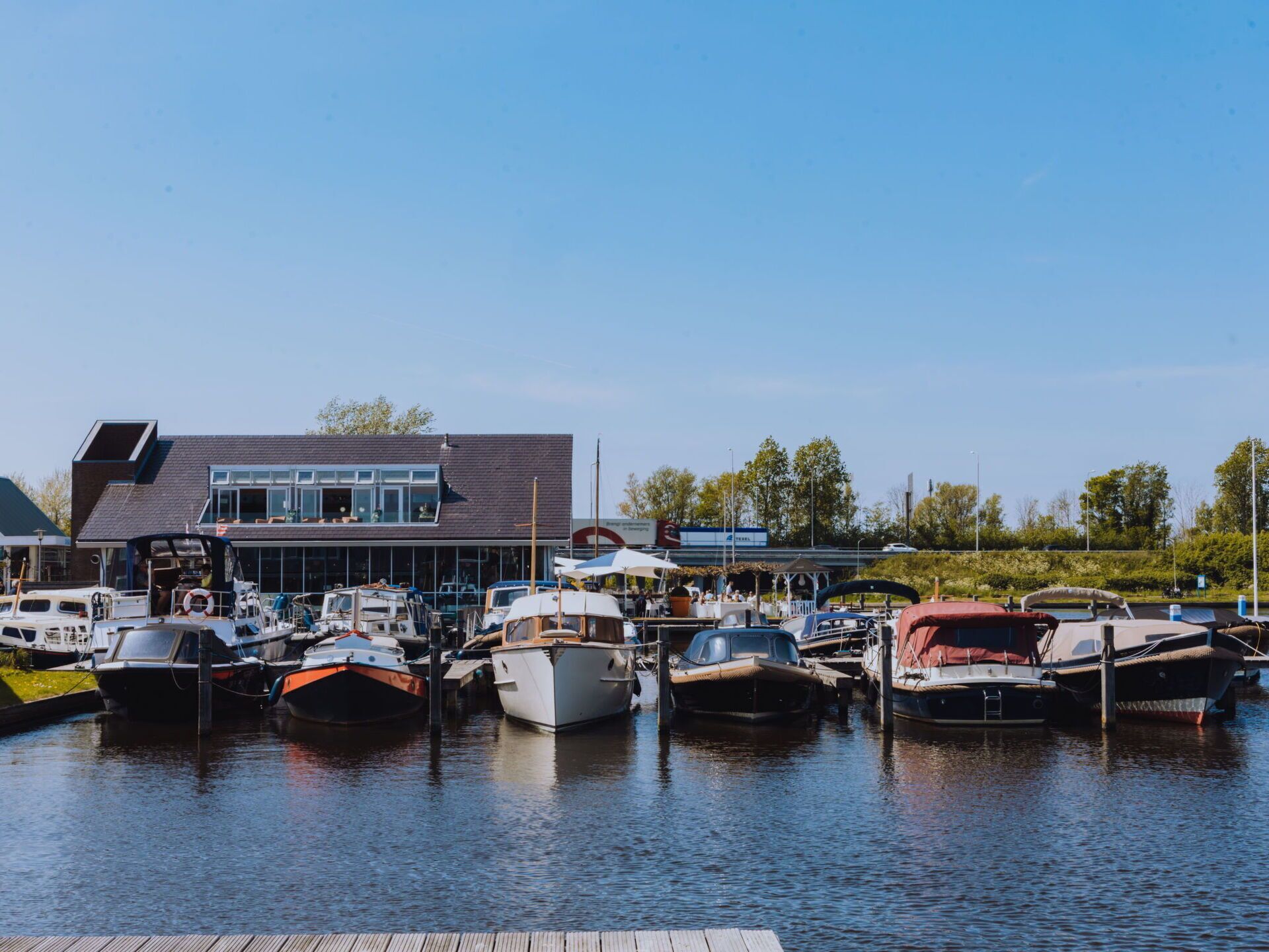 A marina with boats docked, a building with large windows, and a clear sky.
