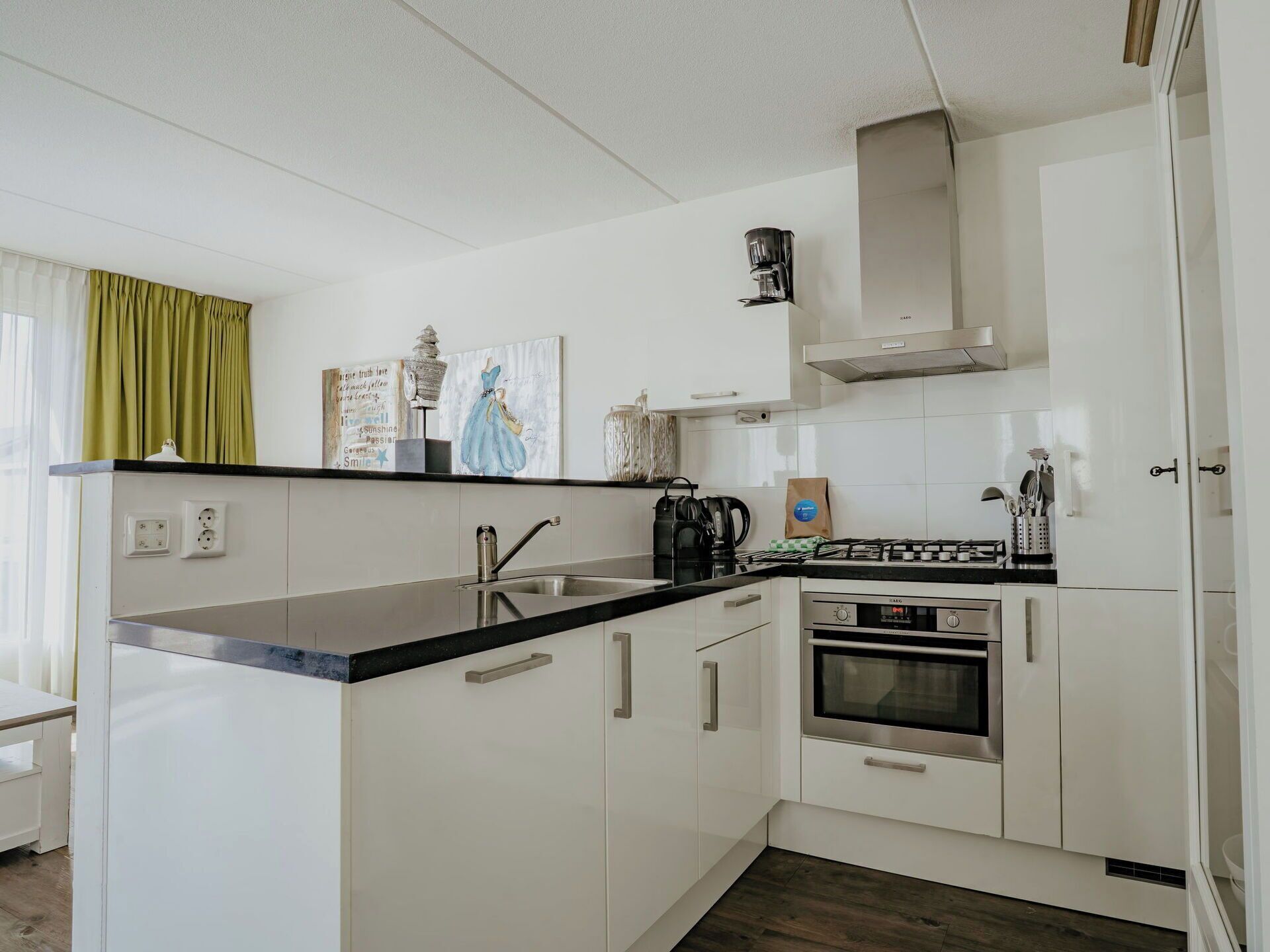 A modern kitchen with white cabinets, a black countertop, a gas stove, an oven, and a coffee maker.