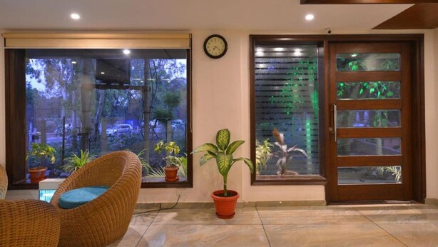 A room with a large window, a clock, a door with frosted glass panels, and a potted plant. - Hotel Pride (Kharar)