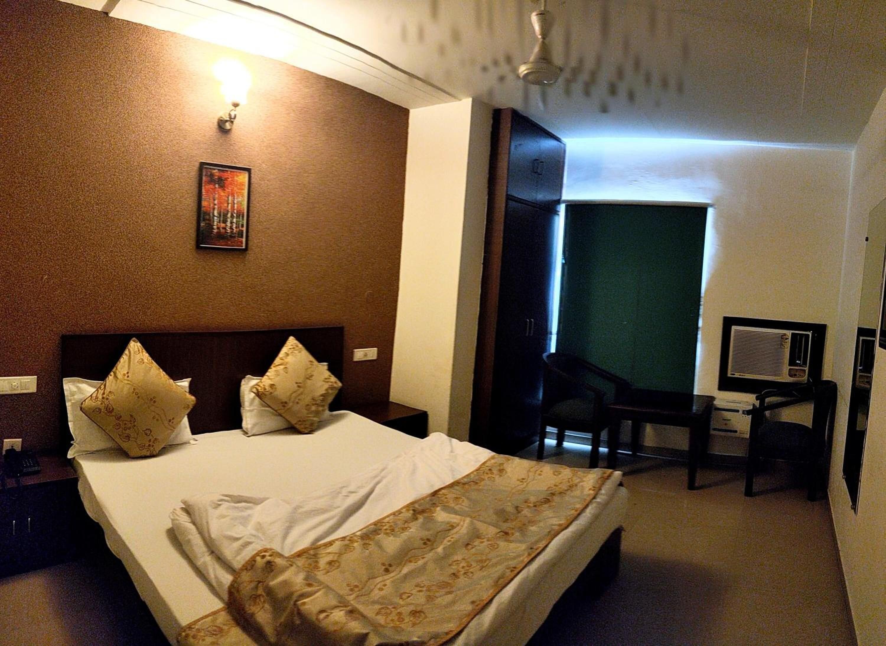 Une chambre d’hôtel avec un grand lit, deux oreillers, un bureau avec une chaise, une lampe de bureau et un tableau au mur.
