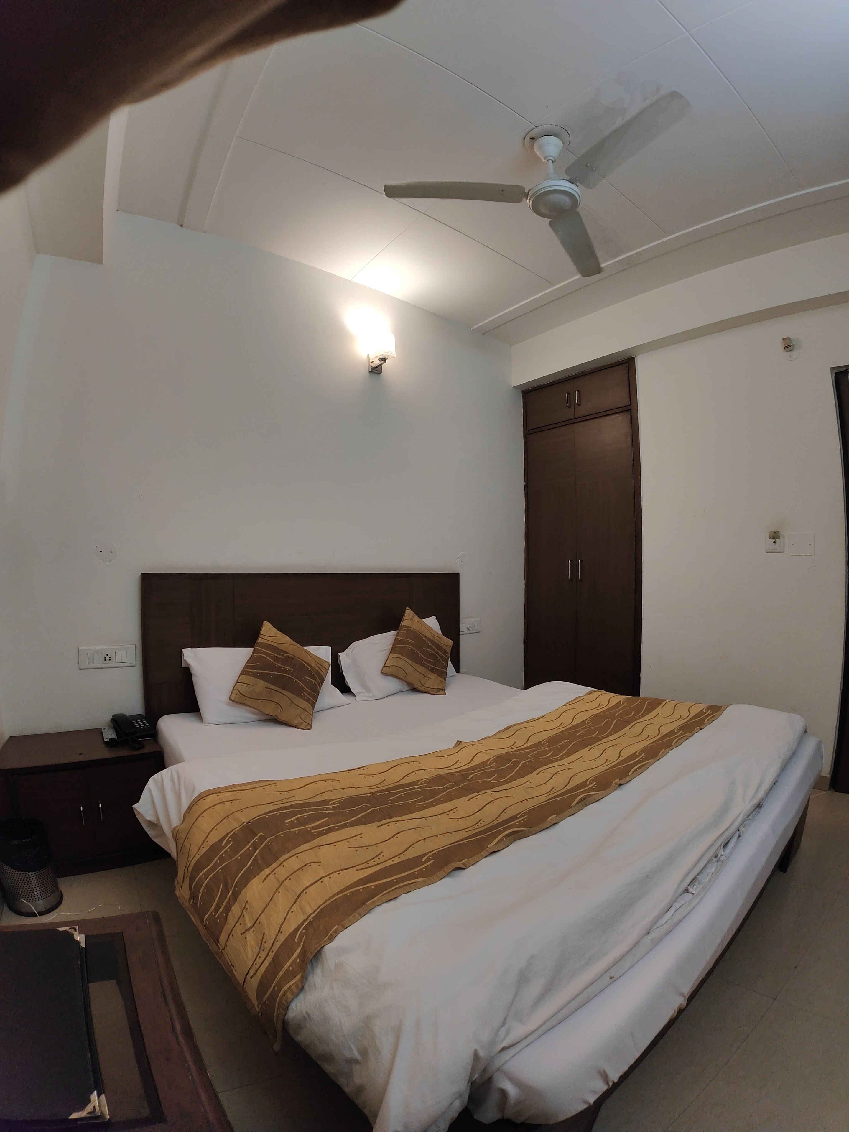 A hotel room with a bed, a nightstand, a telephone, a ceiling fan, and a wardrobe.