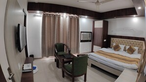 A hotel room with a bed, a desk, a chair, a television, a ceiling fan, and curtains. - Hotel Pride (Kharar)