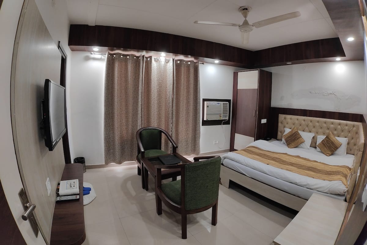 A hotel room with a bed, a desk, a chair, a television, a ceiling fan, and curtains.