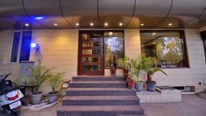 A building entrance with a set of steps leading to a door, potted plants, and a scooter parked outside. - Hotel Pride (Kharar)