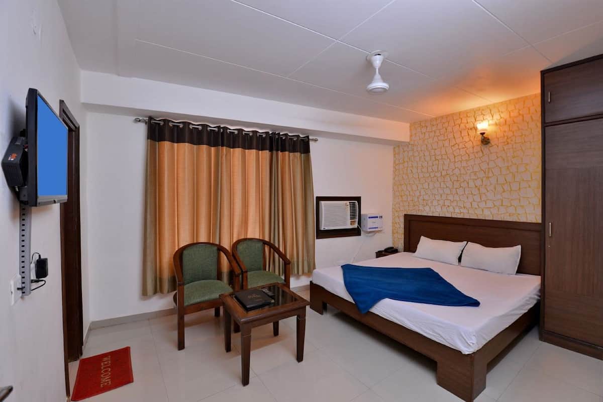 A hotel room with a bed, two chairs, a TV, and a ceiling fan.