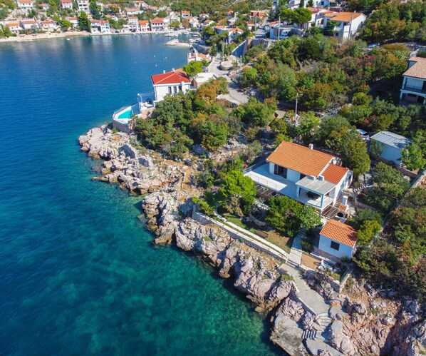 A coastal property with multiple buildings, clear blue waters, rocky shoreline, and lush greenery.