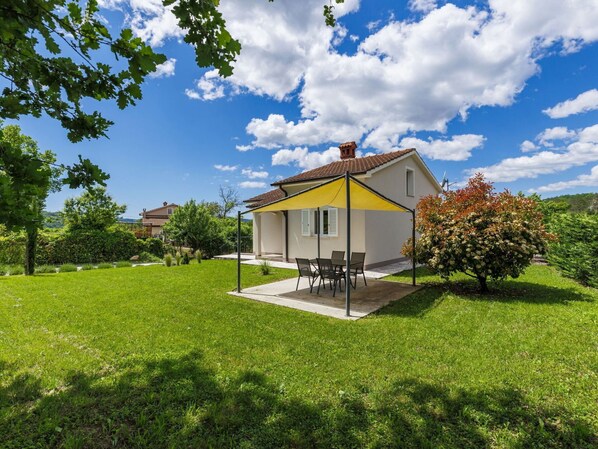 A small house with a patio, surrounded by a well-maintained lawn and trees.
