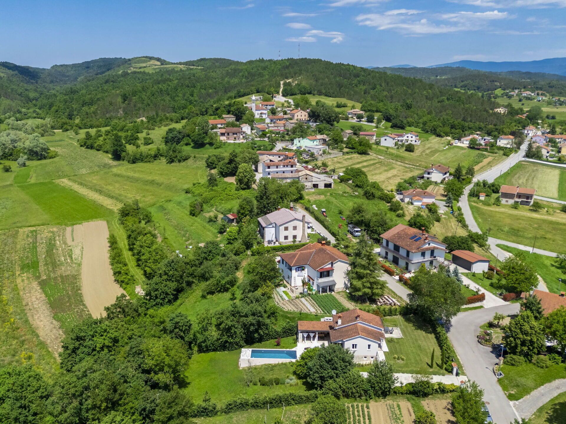 A rural village with houses surrounded by green fields and hills.
