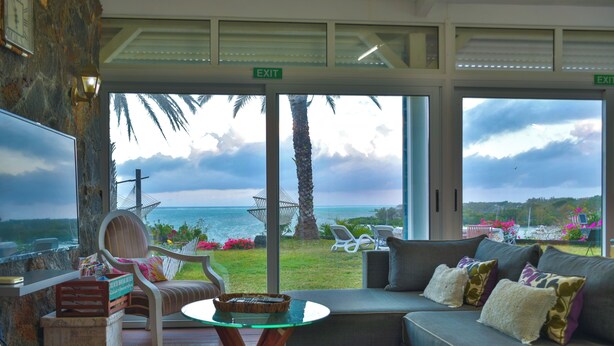 A room with a large window overlooking the sea, a sofa, a chair, and a small table. - Boutique vllla on the rocks (Trou d'Eau Douce)