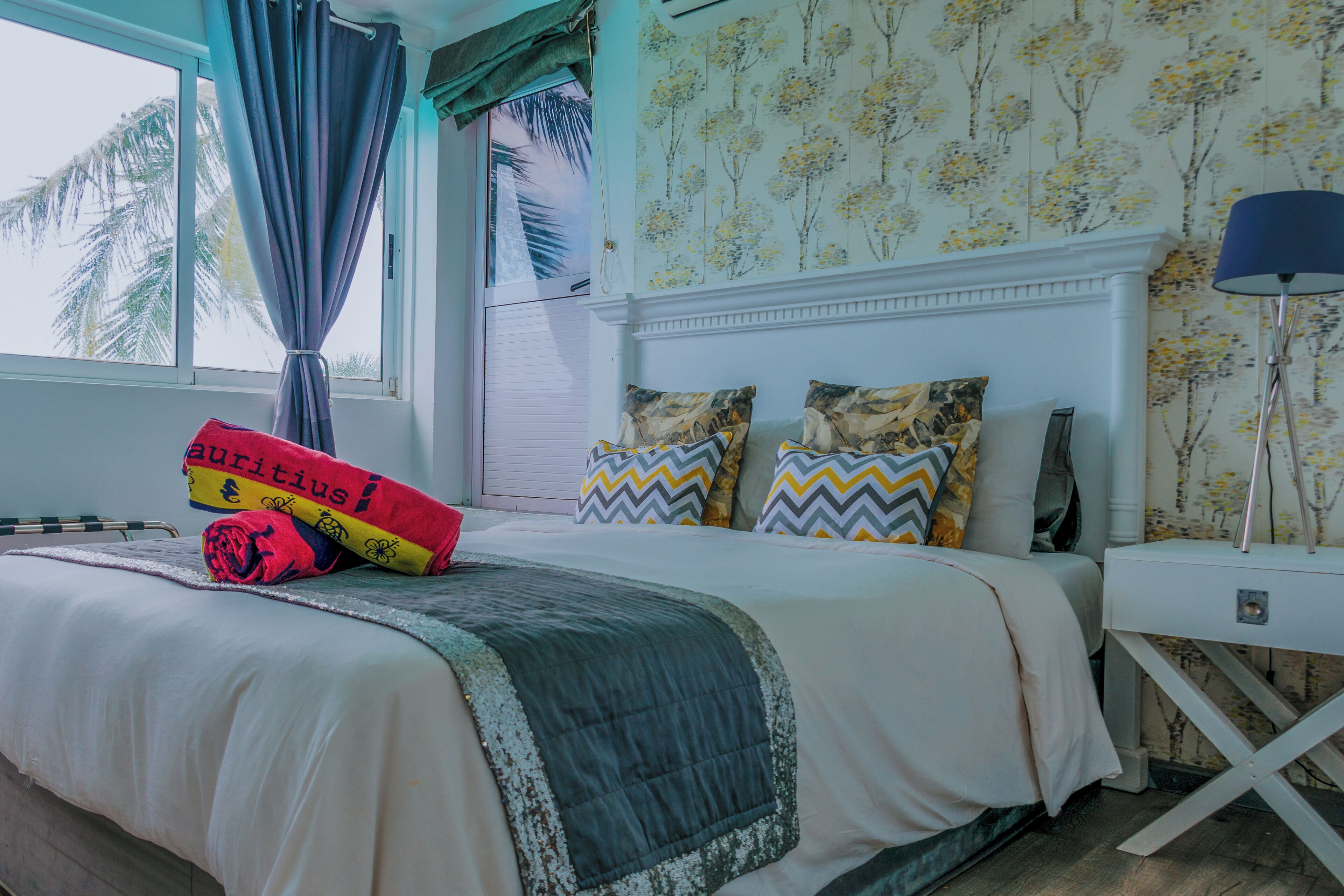 A bedroom with a bed, a nightstand, a lamp, and a window with curtains.