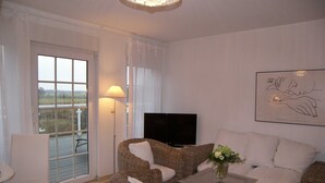 A living room with wicker furniture, a flat-screen TV, and a framed artwork on the wall.