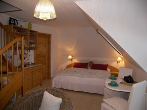 A cozy attic bedroom with a wooden staircase, a bed with white bedding, two bedside lamps, and a small table with a teapot and cups.