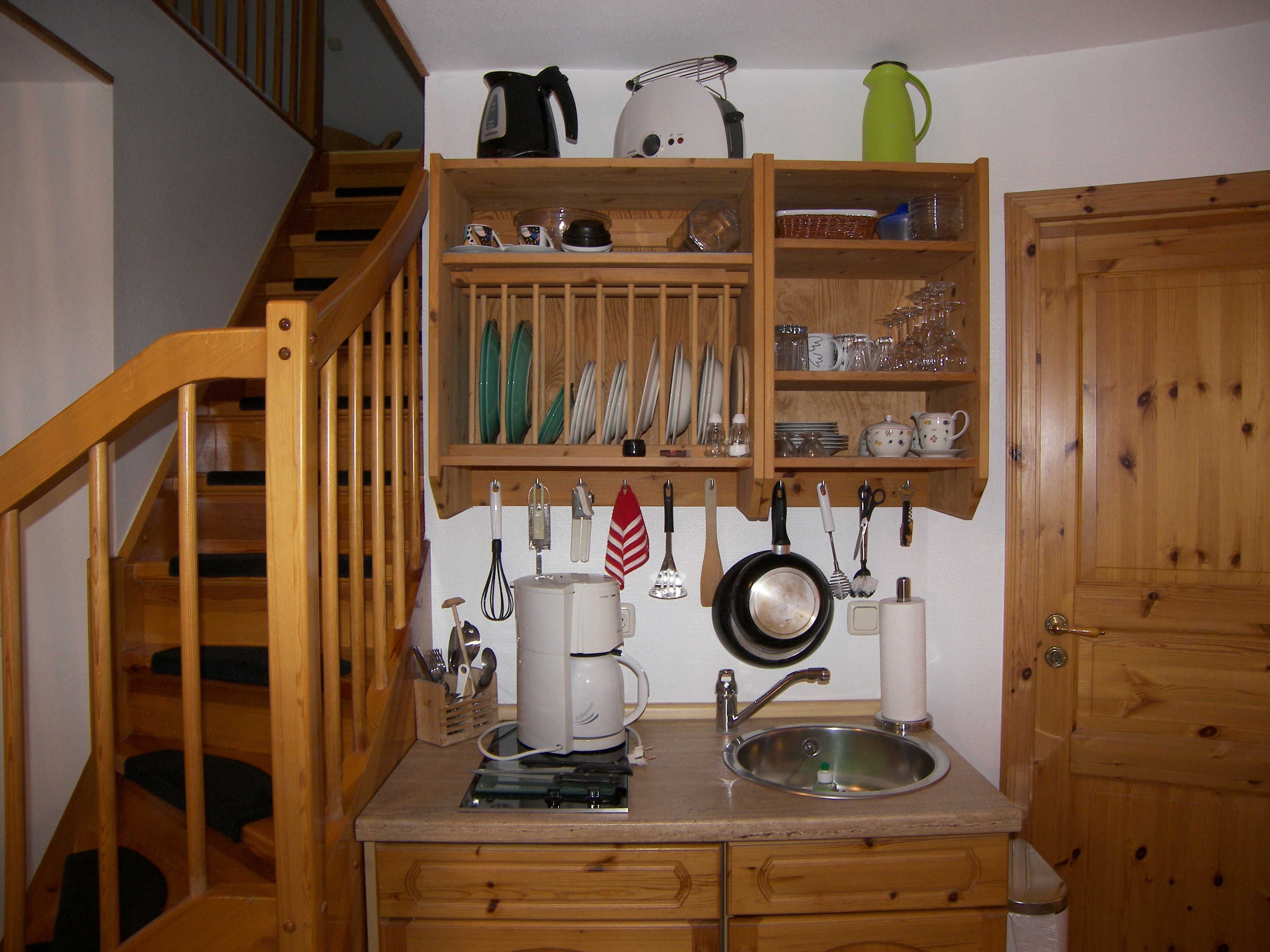 Een compacte keuken met houten kastjes, een ingebouwd spoelgedeelte en diverse keukengerei en pannen die aan de muur hangen.