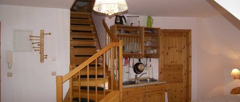 A cozy room with a wooden staircase, a dining area with wooden cabinets, and a bed with a striped blanket.